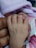 A baby's hand gently holds onto an adult's finger, with a background of soft pink fabric. The scene conveys a sense of tenderness and connection.