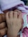 A baby's hand gently holds onto an adult's finger, with a background of soft pink fabric. The scene conveys a sense of tenderness and connection.