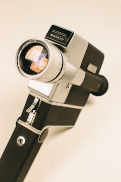 A vintage handheld video camera with a metallic and black exterior, featuring a large lens and several controls visible on its body. The camera displays the brand name on top, giving it a classic and retro appearance.