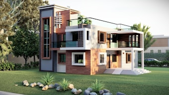 A modern two-story house with a sleek design featuring a mix of wood and glass elements. The facade includes large windows and balconies with glass railings. The surroundings are lush with well-maintained grass, rocks, and various trees.