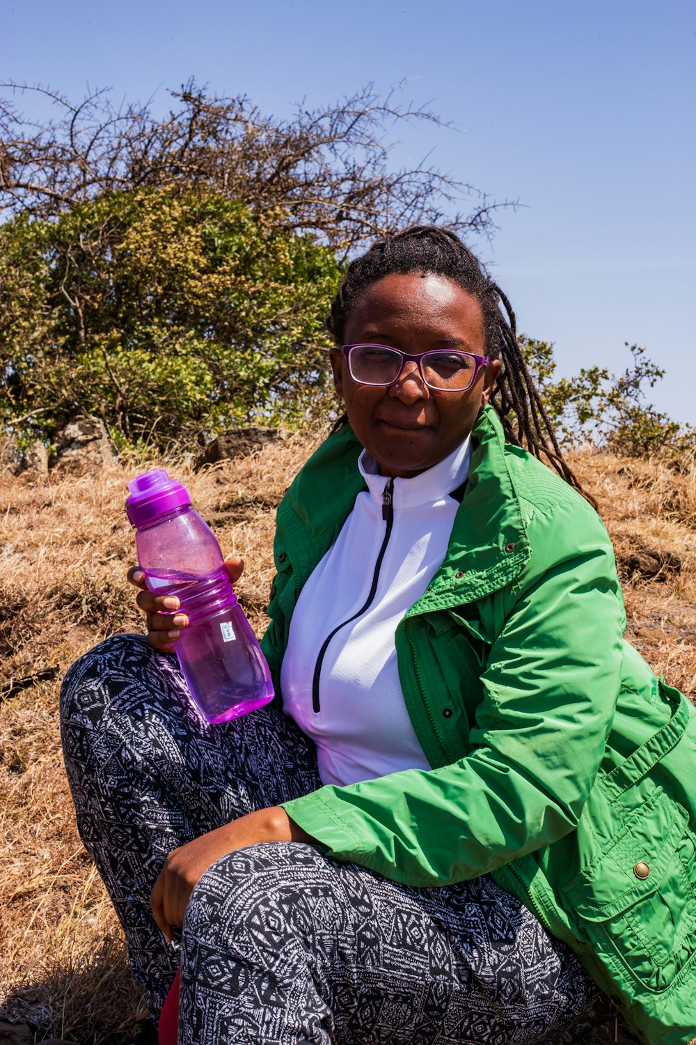 woman in green jacket holding purple plastic bottle