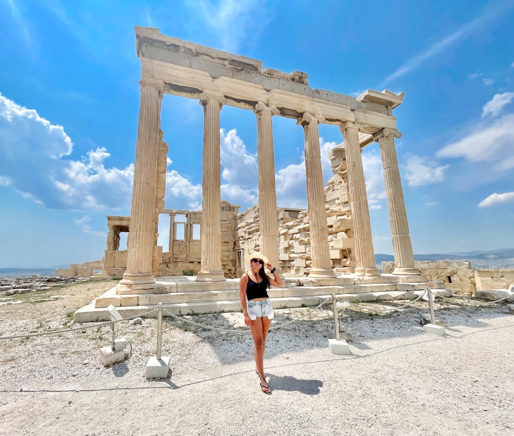 woman in black tank top and blue denim shorts standing near brown concrete building during daytime