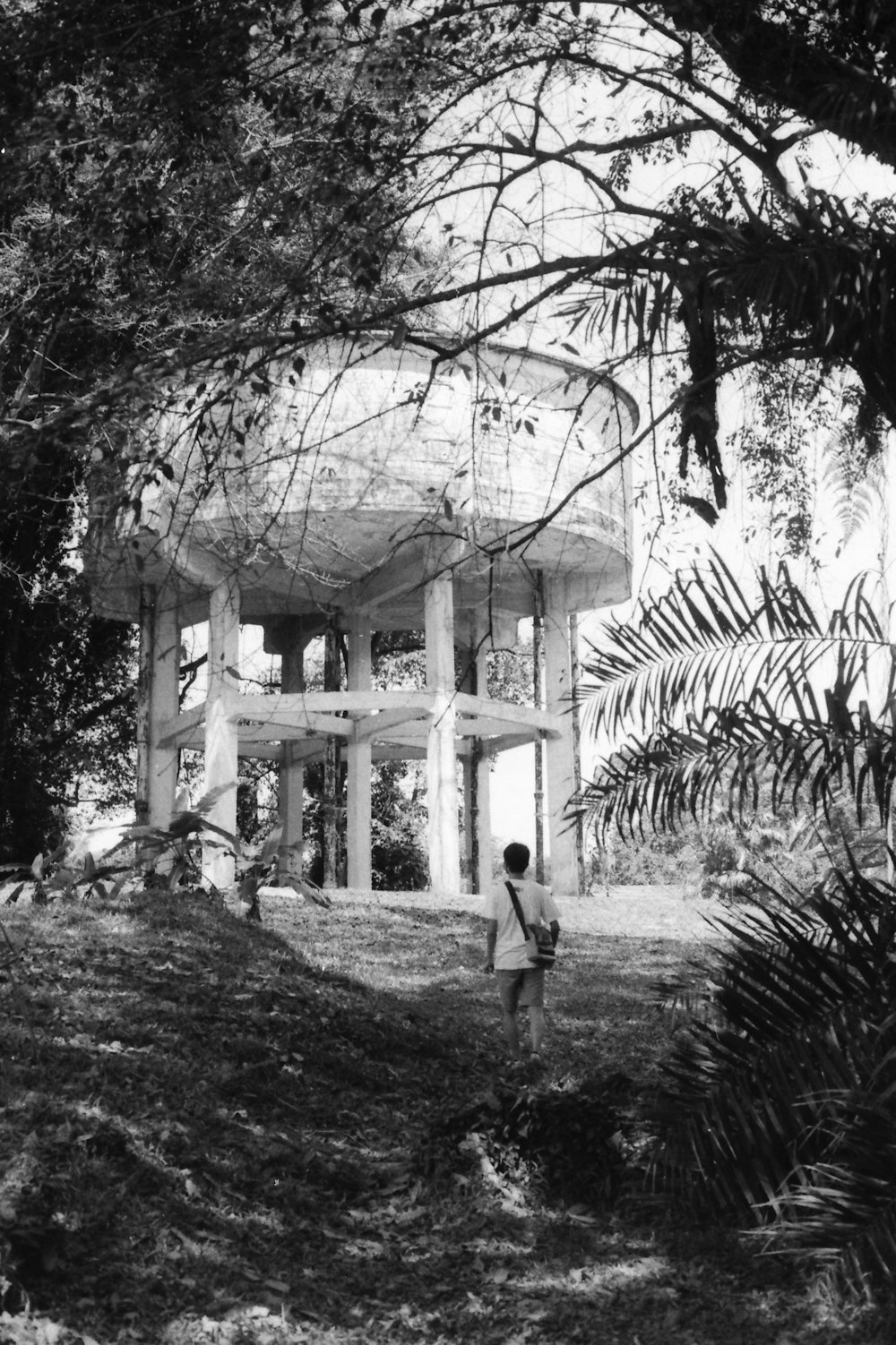 grayscale photo of man in black jacket and pants standing near building