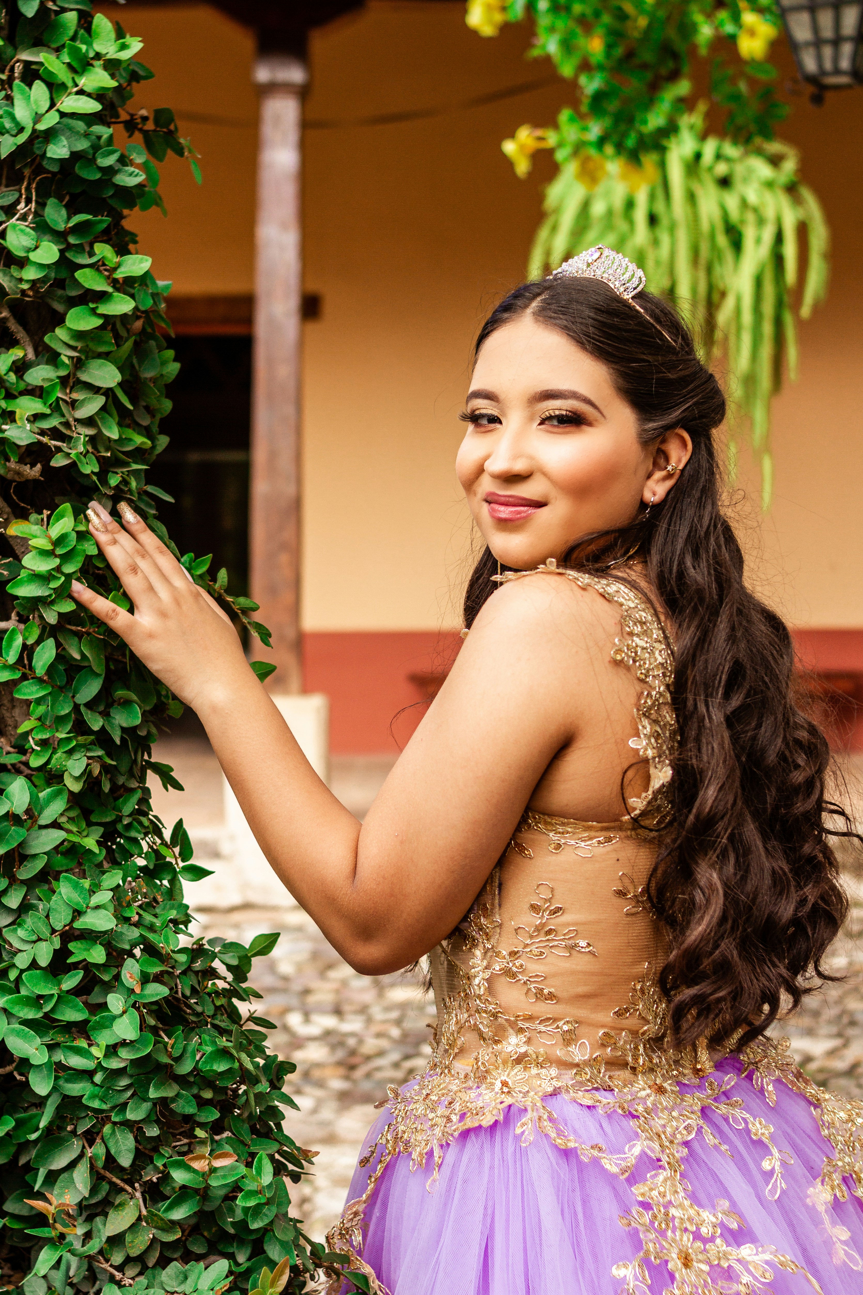 woman in gold floral dress standing beside green plant
