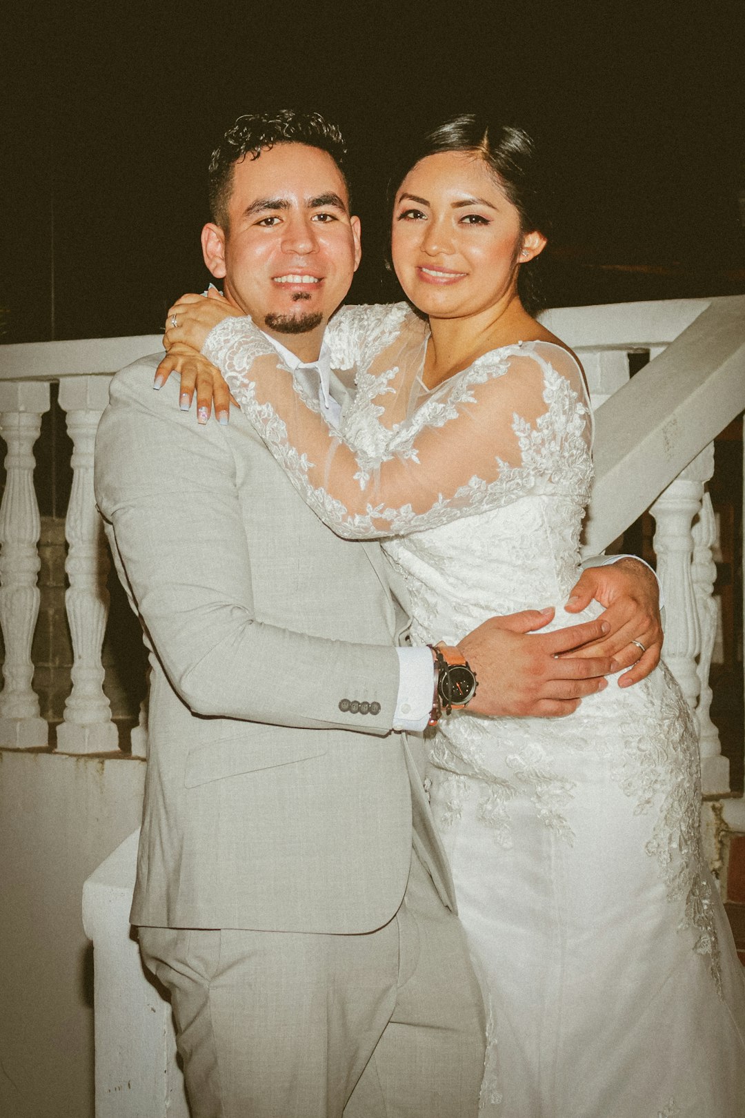 man in gray suit hugging woman in white lace long sleeve dress