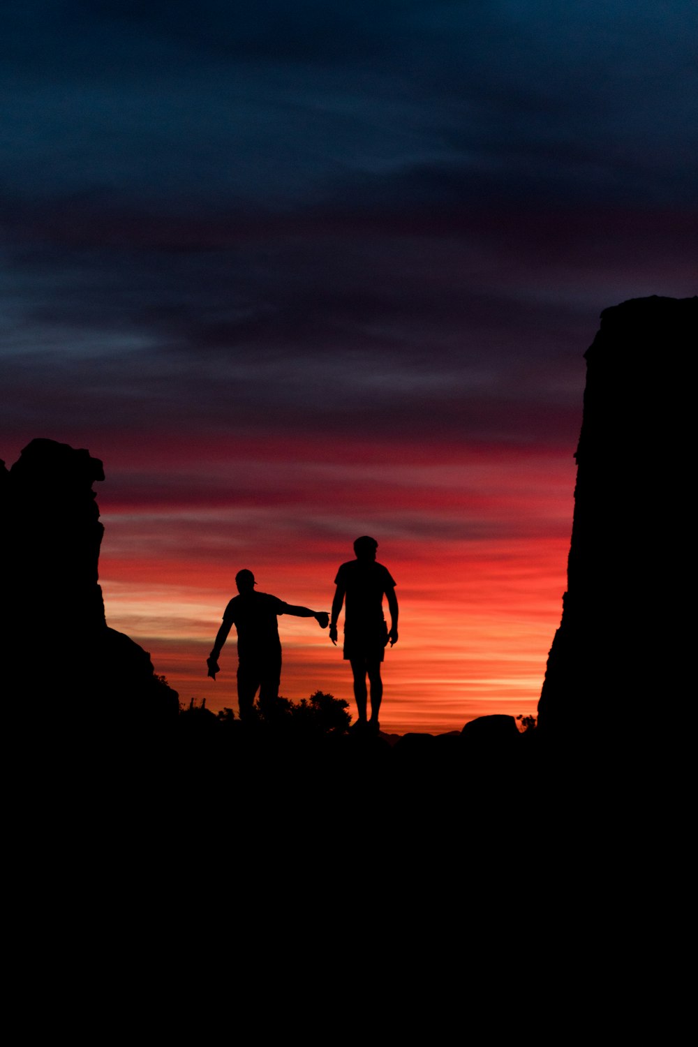 silhouette of people standing on rock formation during sunset