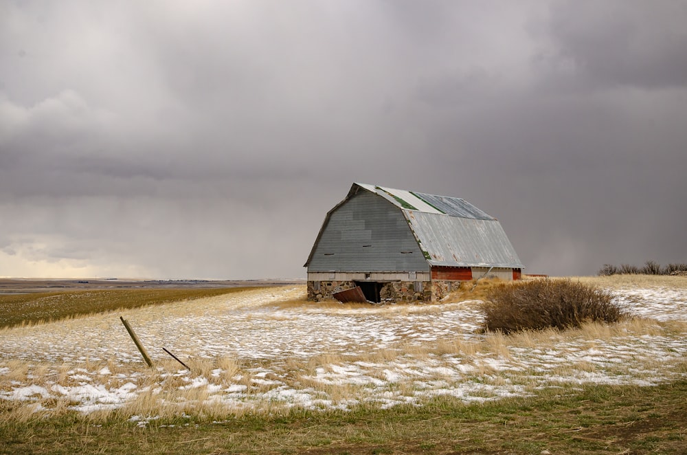 brown wooden barn on brown field under gray cloudy sky