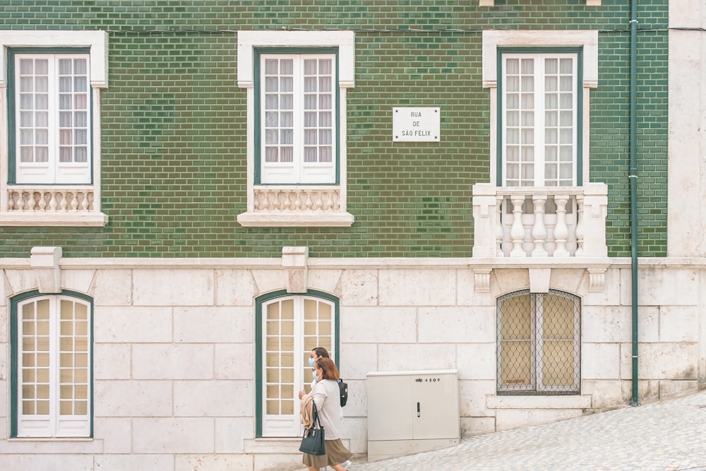 woman in black jacket and blue denim jeans standing near green concrete building during daytime