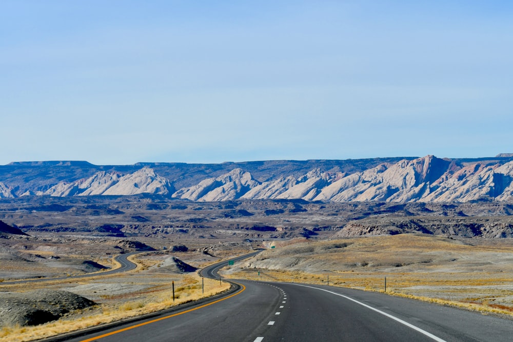 gray concrete road near brown mountain under white sky during daytime