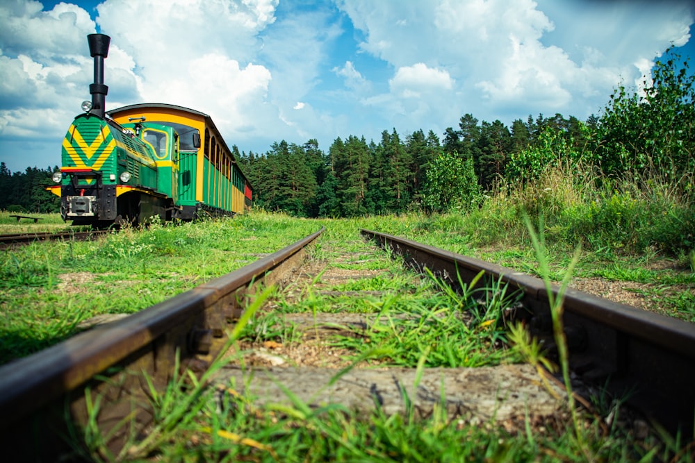 yellow and black train on rail tracks near green trees under white clouds and blue sky