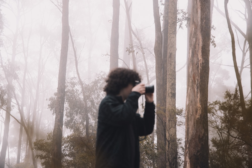 woman in black coat taking photo of trees during daytime