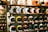 A display of colorful motorcycle helmets arranged on wooden shelves, showcasing various designs and styles. The helmets feature artistic patterns, including checkerboard and flame motifs, and are placed on multiple levels.