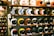 A display of colorful motorcycle helmets arranged on wooden shelves, showcasing various designs and styles. The helmets feature artistic patterns, including checkerboard and flame motifs, and are placed on multiple levels.