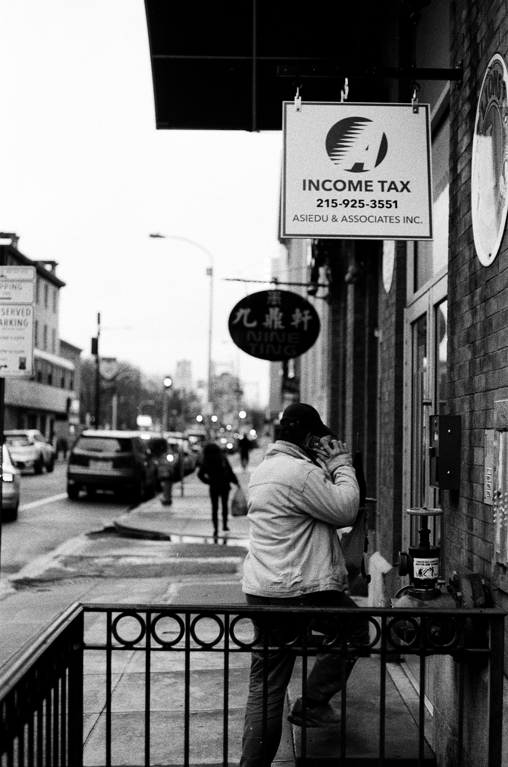 grayscale photo of man in white shirt standing near road sign