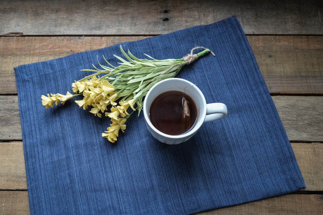 white ceramic mug with brown liquid, Morning cup of tea with yellow flowers on the table
