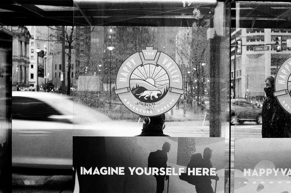 grayscale photo of man standing in front of glass window