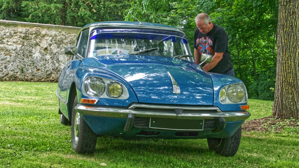 man in black t-shirt standing beside blue car