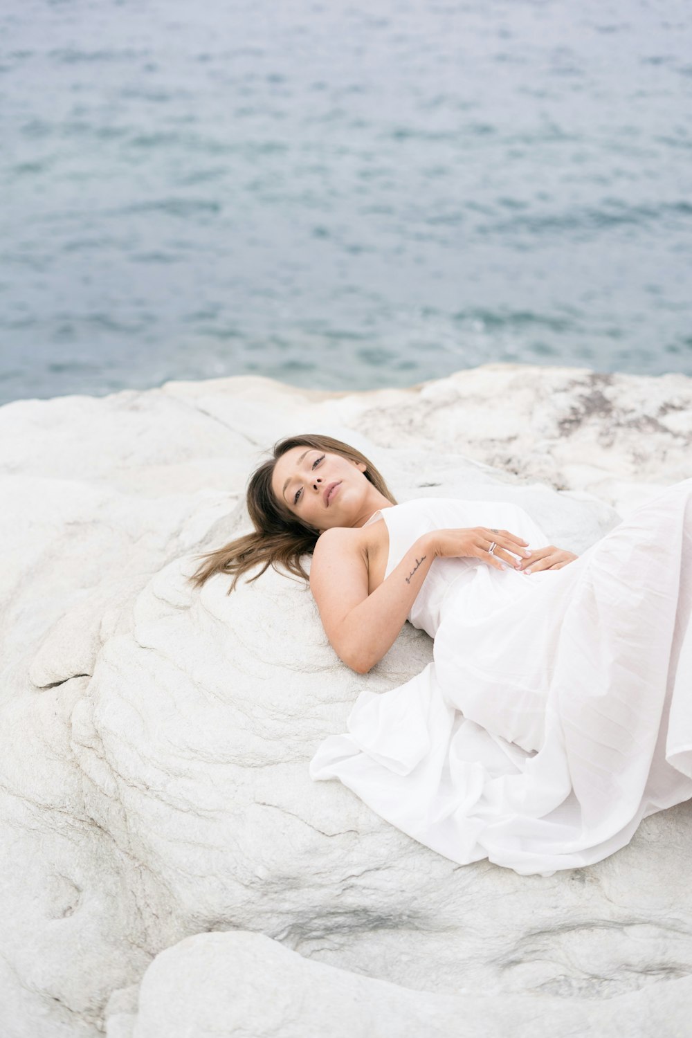 woman in white dress lying on white sand beach during daytime