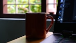 A moody photo of a glowing deep purple coffee mug beside a laptop in dark mode.