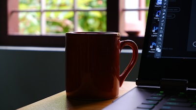 A moody photo of a glowing deep purple coffee mug beside a laptop in dark mode.