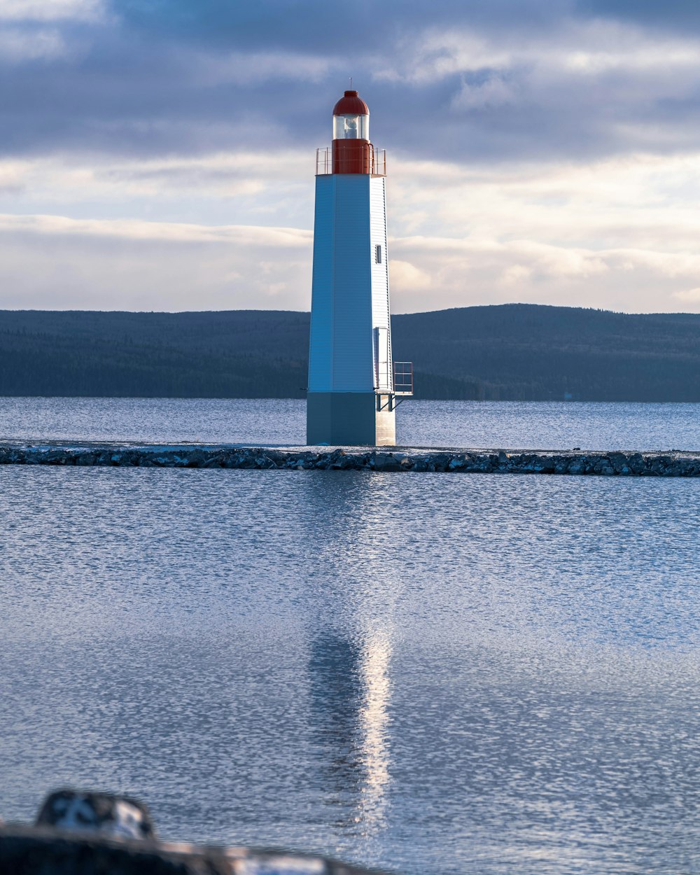 white and red lighthouse on body of water under cloudy sky during daytime