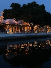 Cozy outdoor dining area beside a flowing river at sunset with string lights overhead.