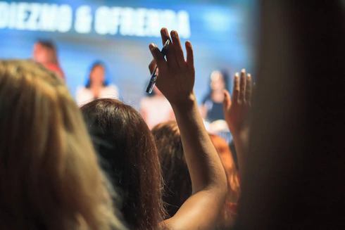 People in an audience raising their hands to ask questions at a conference