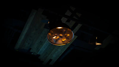 A heavy industrial pendant light with a dark steel finish glowing warmly against a black backdrop.