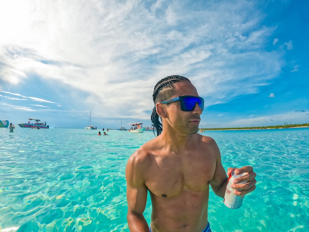 topless man in blue shorts wearing black sunglasses holding clear plastic bottle