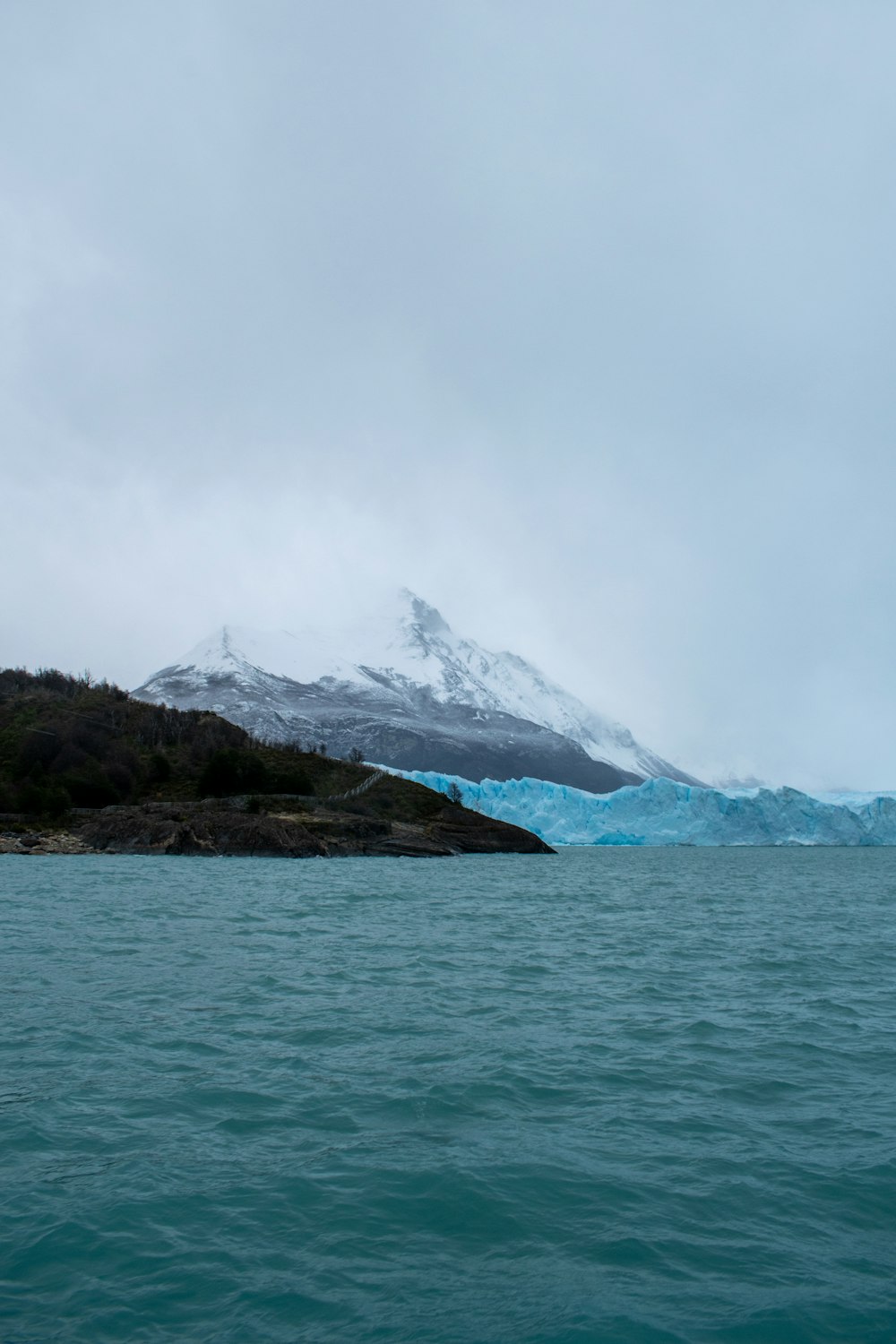 body of water near mountain under white sky during daytime