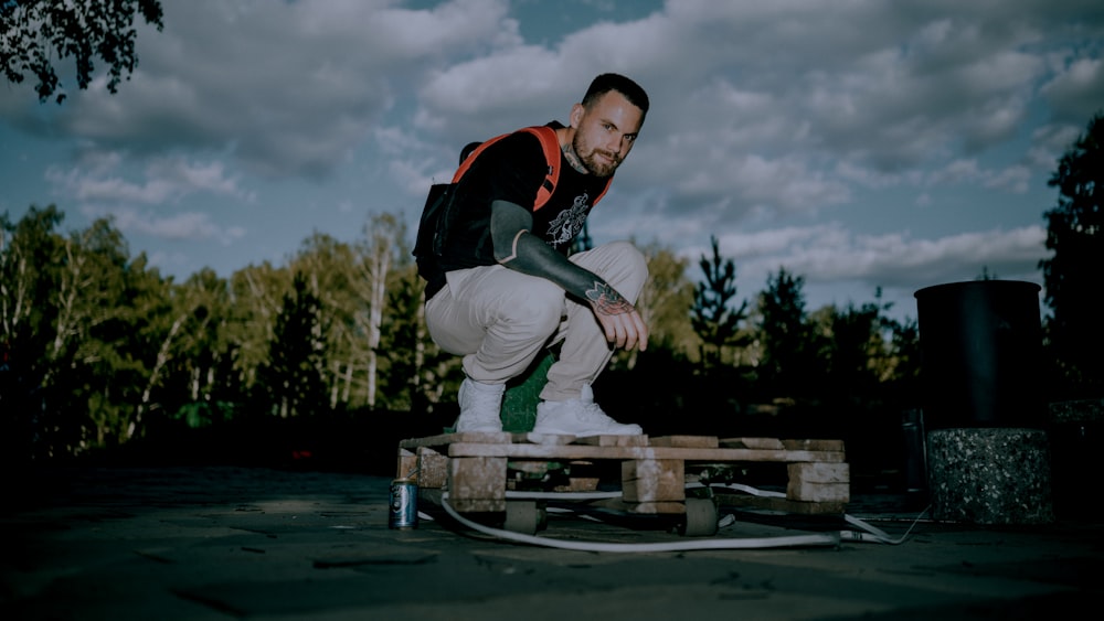 man in black and red jacket and white pants sitting on brown wooden bench during daytime