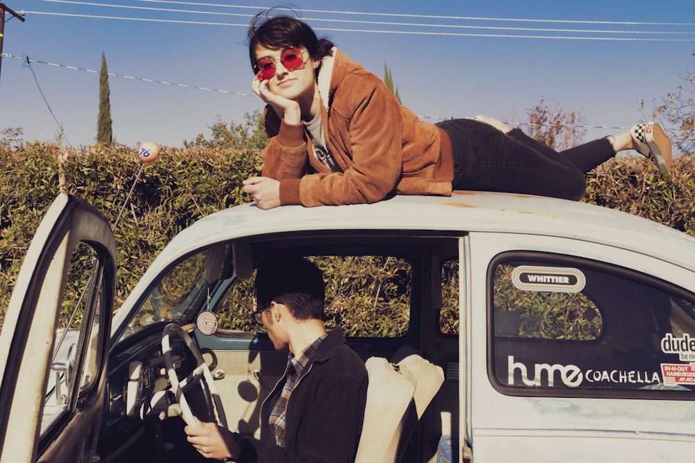 man in brown jacket sitting on white car