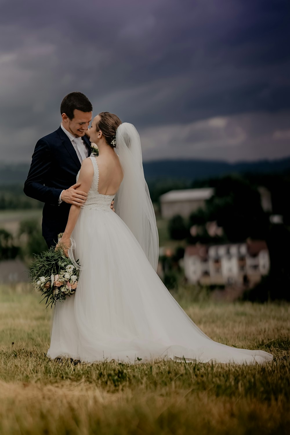 man in black suit kissing woman in white wedding dress on green grass field during daytime