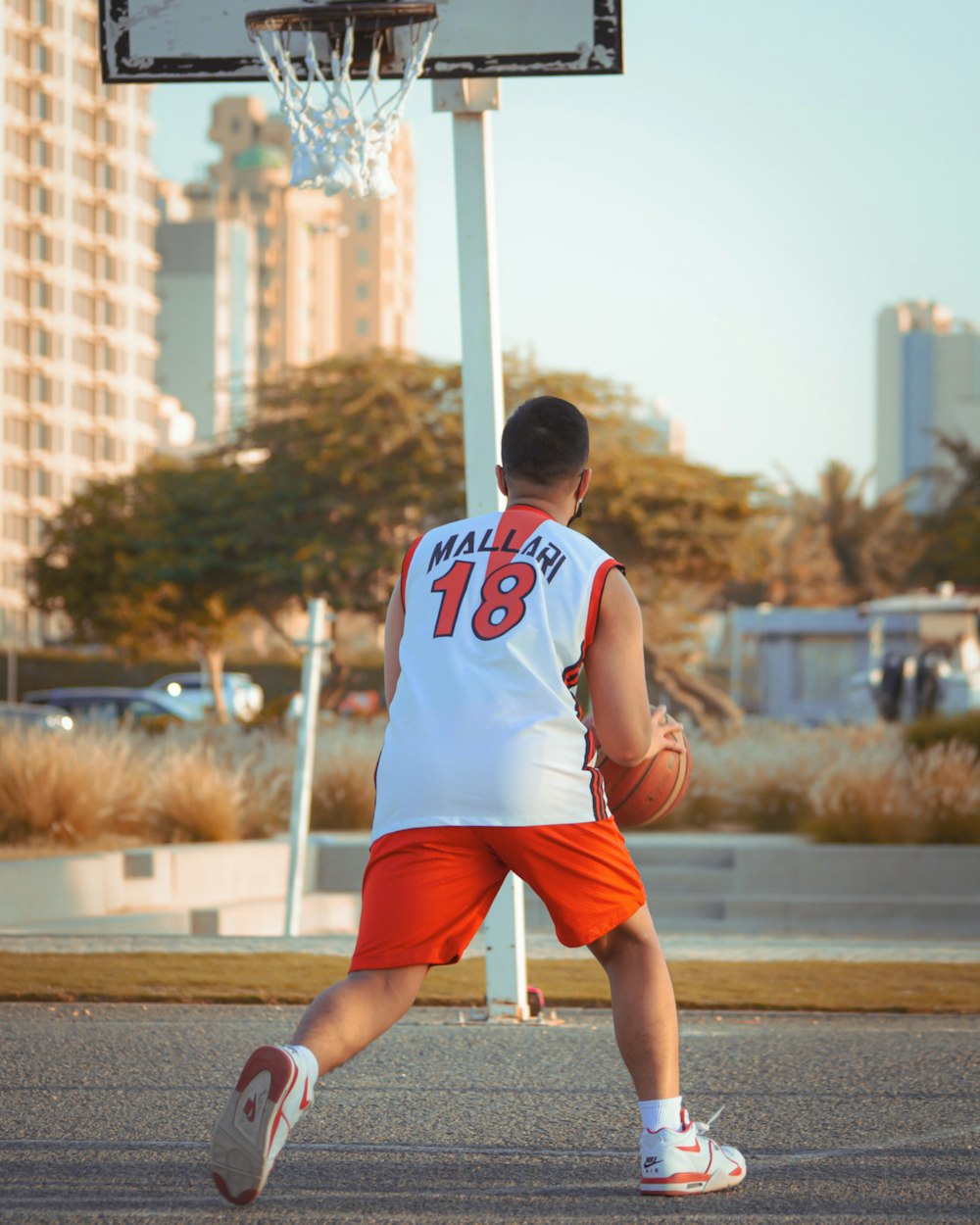 man in white and orange jersey shirt and red shorts running on road during daytime