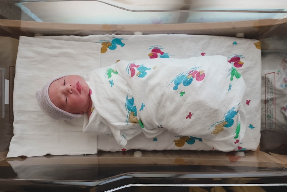 baby in white and red floral onesie lying on bed