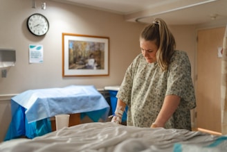pregnant woman in gray and white hospital gown standing beside bed