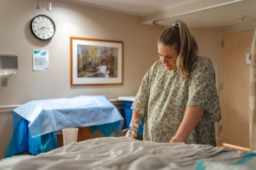 pregnant woman in gray and white hospital gown standing beside bed