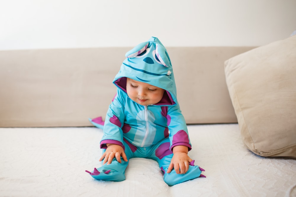 child in green and pink hoodie sitting on white couch