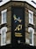 The corner of a brick building features a large, vertical sign with elegant writing in both English and another script, reading 'Persian Kitchen'. Above the text, an artistic illustration shows two birds perched on a branch with pomegranates. The building is located at the intersection of Bonchurch Road and Portobello Road.