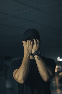 man in black crew neck t-shirt covering face with hands