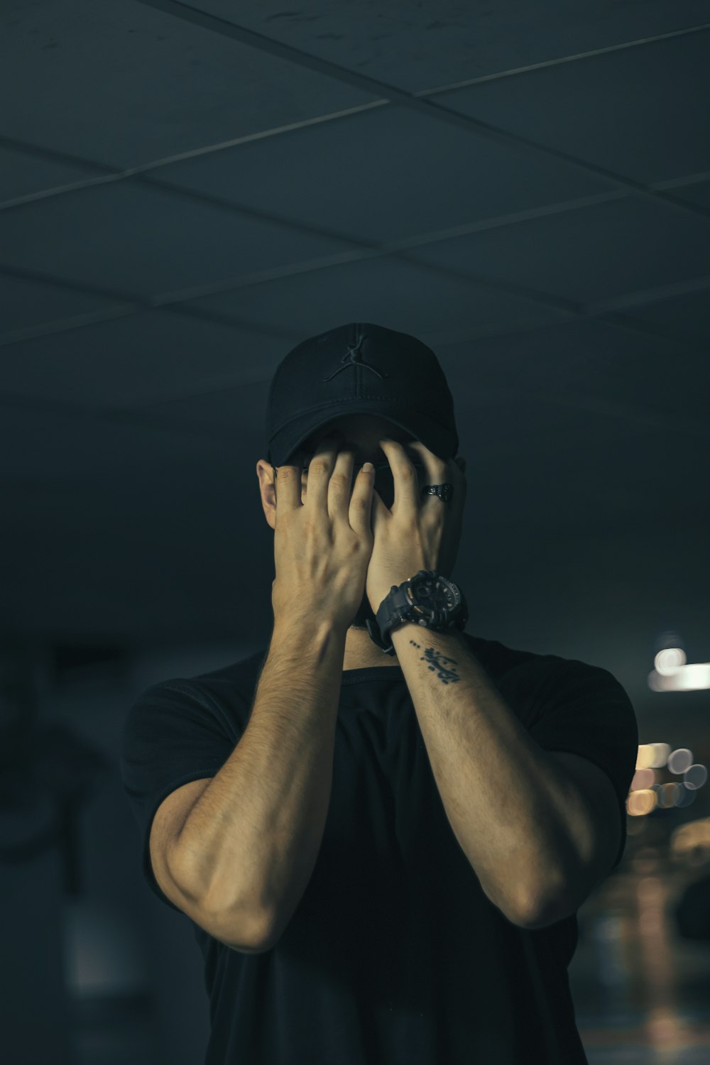 uomo in t-shirt girocollo nera che copre il viso con le mani