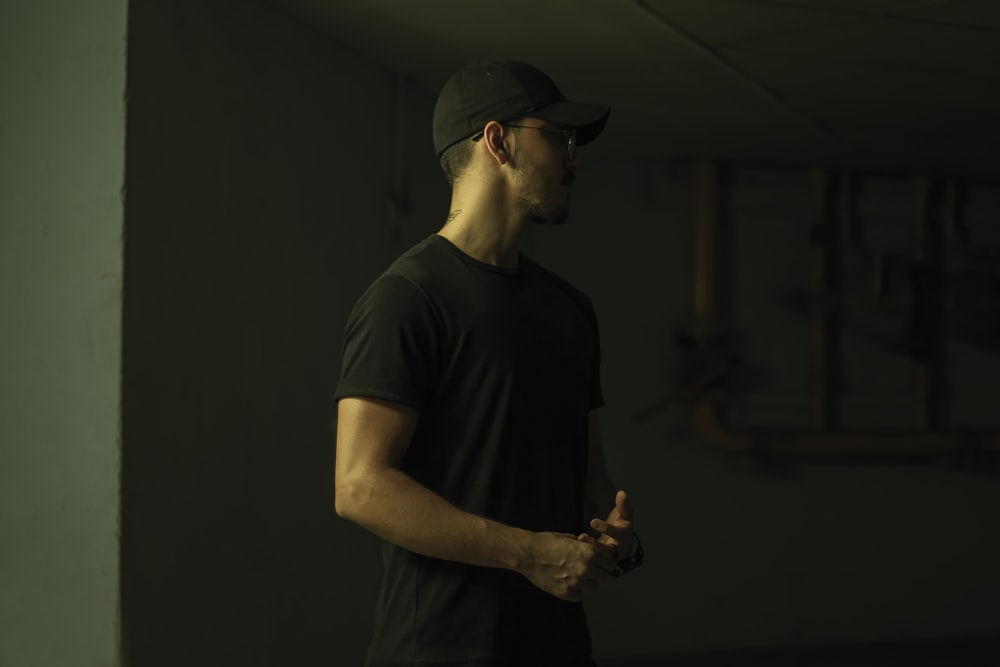 man in black crew neck t-shirt wearing black cap holding black smartphone