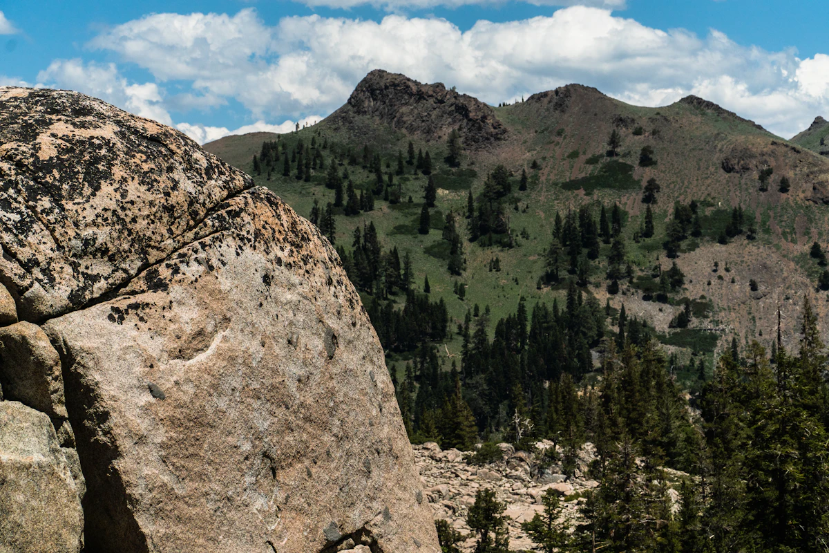 A granite boulder in front of a forested ridge and rocky summits in Olympic Valley