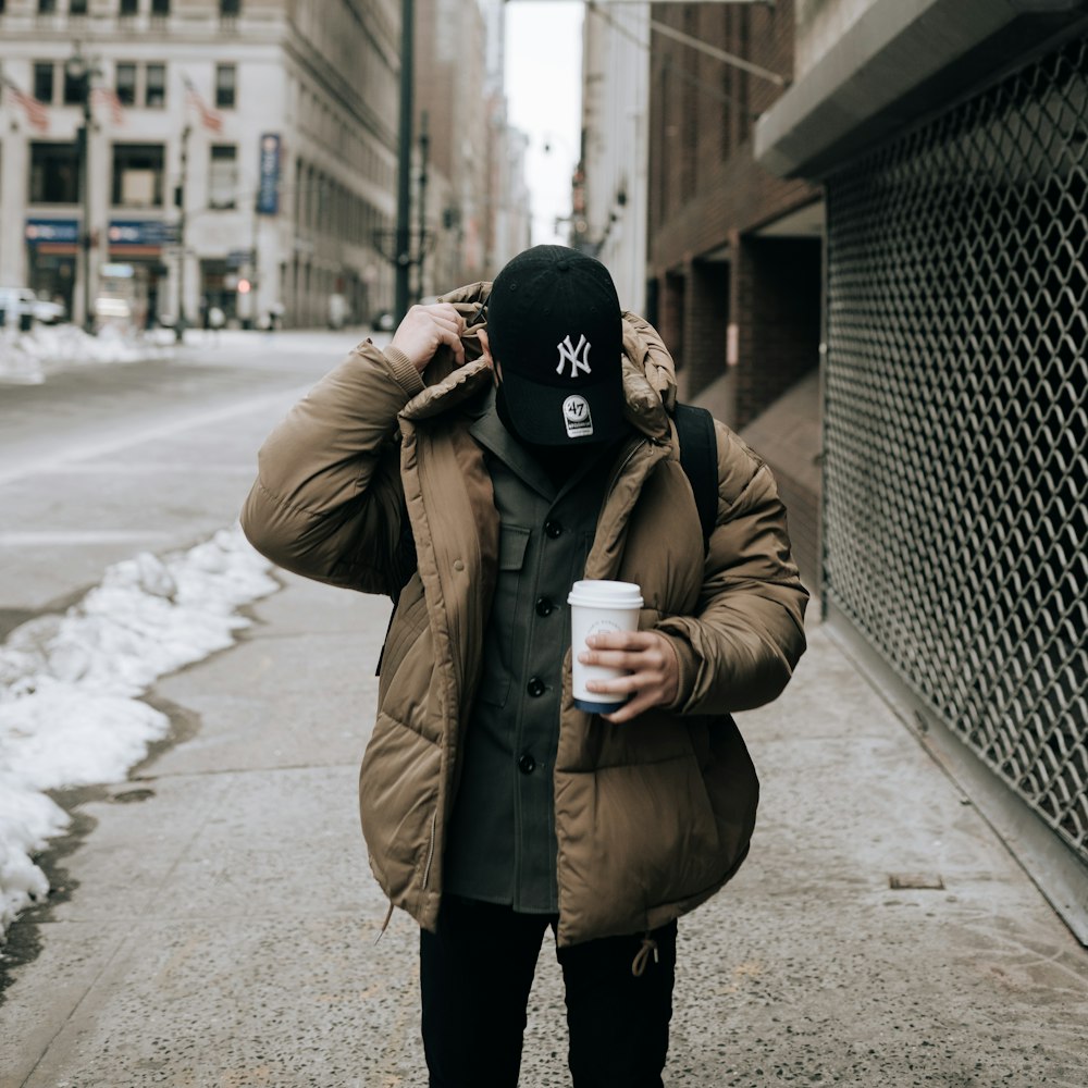 woman in brown coat and black knit cap standing on sidewalk during daytime