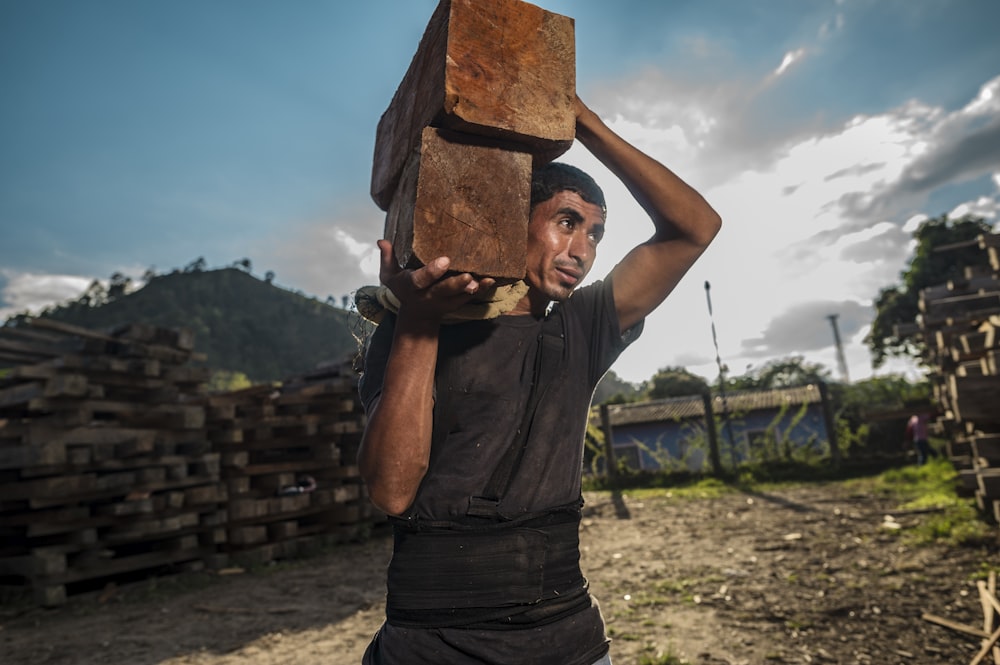 man in gray tank top holding brown wooden board