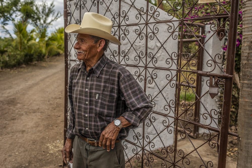 hombre con camisa de vestir a cuadros azul y blanco y pantalones marrones con sombrero de vaquero marrón de pie