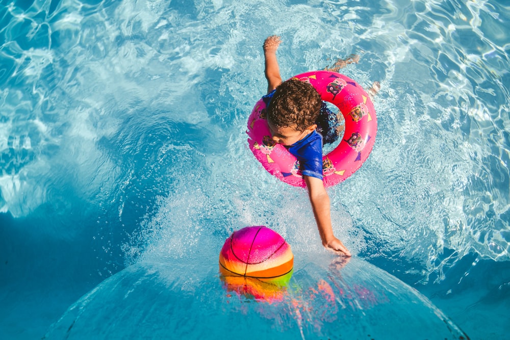 Chica en camiseta sin mangas azul y pantalones cortos azules sosteniendo un anillo inflable rosa en el agua