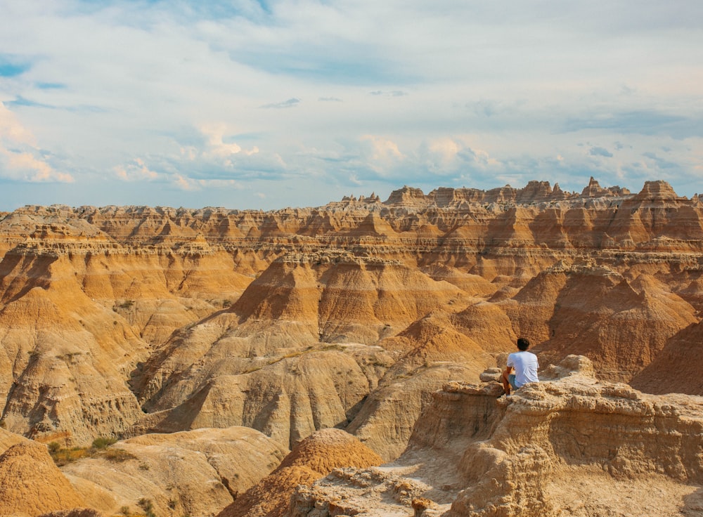 man in white shirt sitting on brown rock formation during daytime