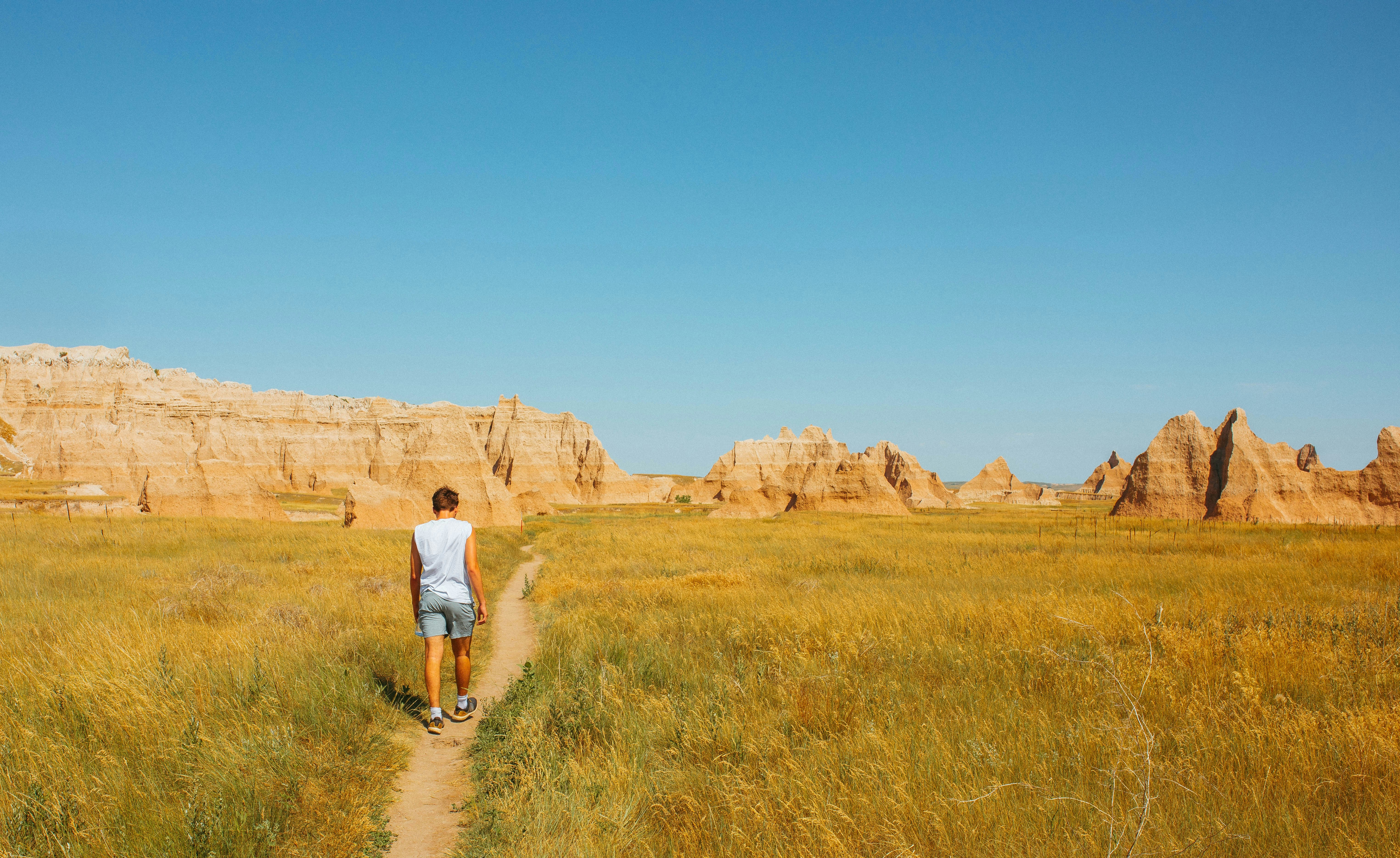 man in white t-shirt and blue denim shorts walking on green grass field during daytime