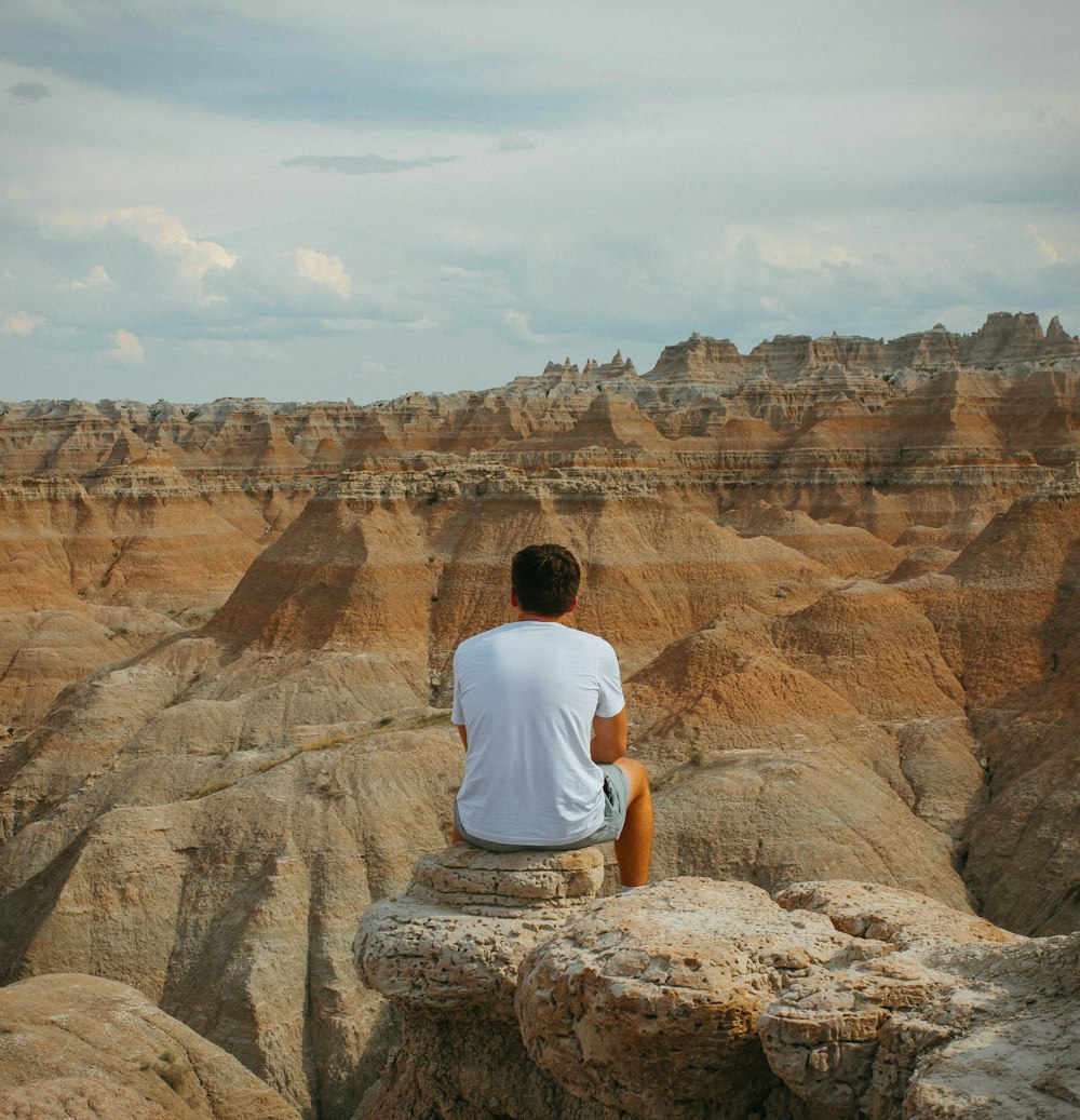 homme en t-shirt blanc assis sur la formation rocheuse brune pendant la journée